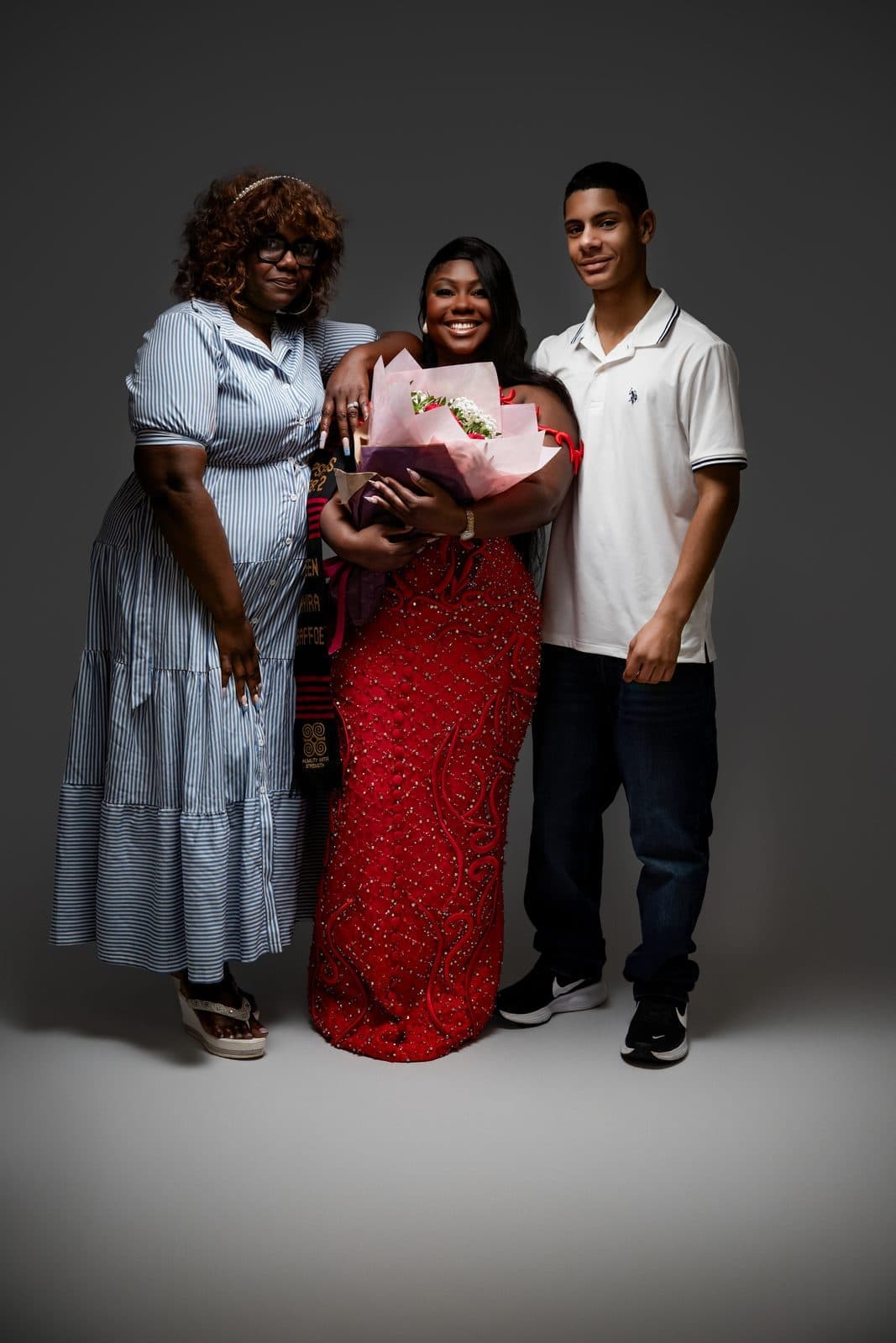 Graduate in red gown with two family members, graduation family portrait in studio