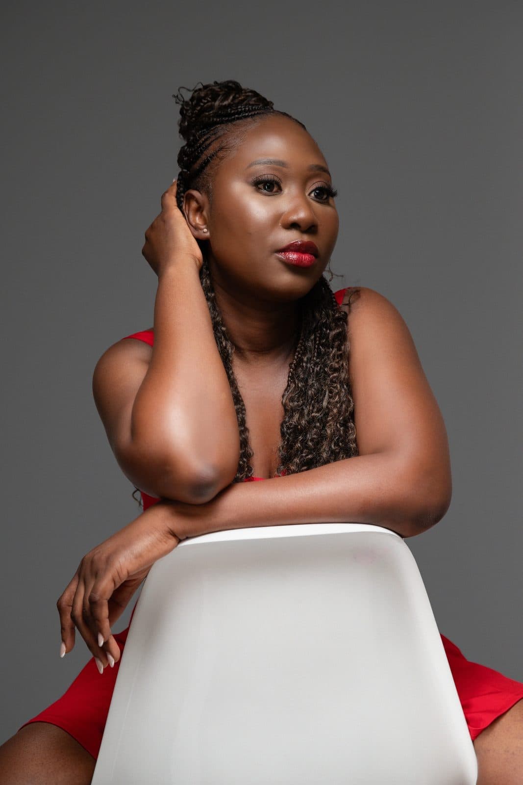 Woman in red dress leaning on a white chair, studio glamour portrait